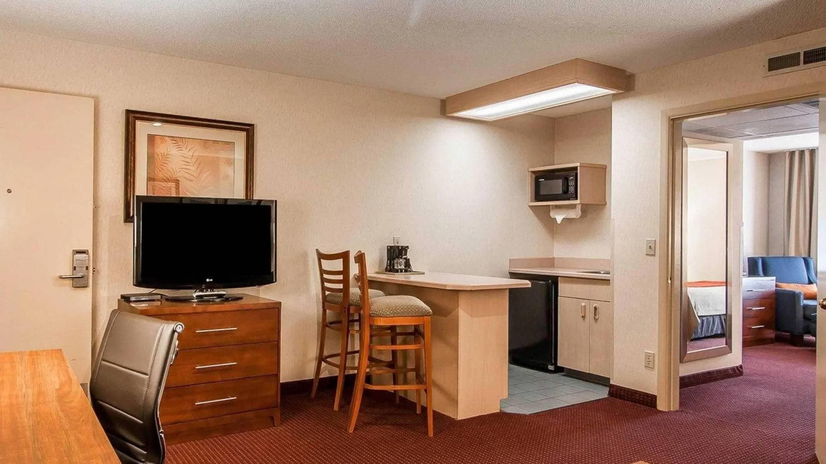 Une chambre d’hôtel compacte équipée d’une télévision, d’une petite kitchenette, d’un coin repas et d’une salle de bain visible à travers une porte ouverte.