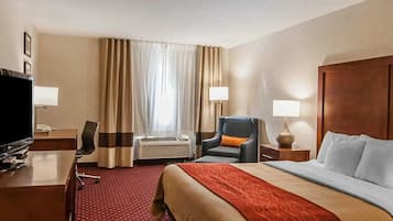 Habitación de hotel con cama, escritorio con televisor, silla, lámpara y ventana con cortinas.