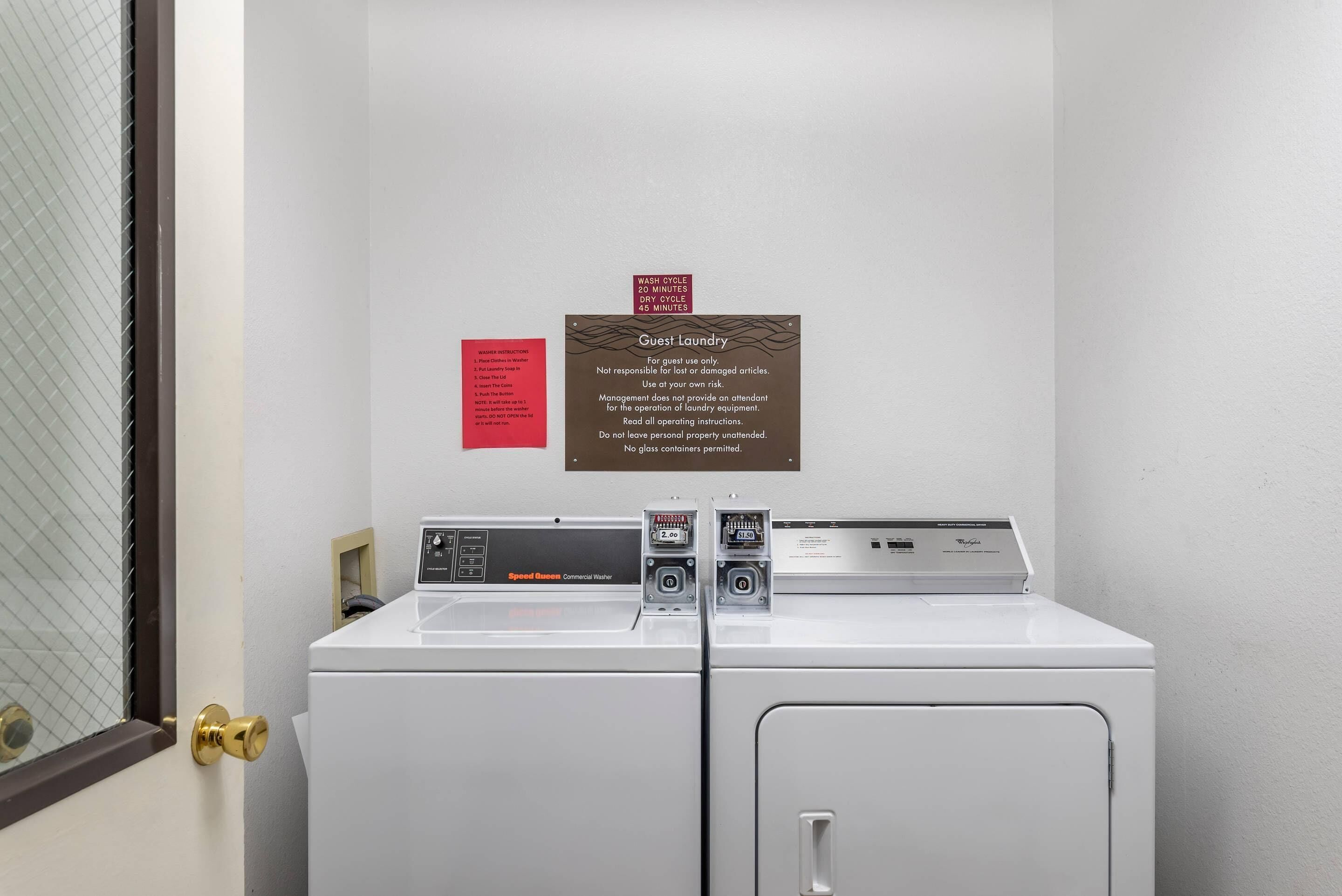 A hotel laundry area with two Speedmaster Commercial Washers, a guest laundry sign, and a door with a brass handle.