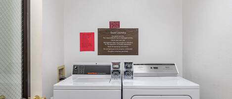 A hotel laundry area with two Speedmaster Commercial Washers, a guest laundry sign, and a door with a brass handle.