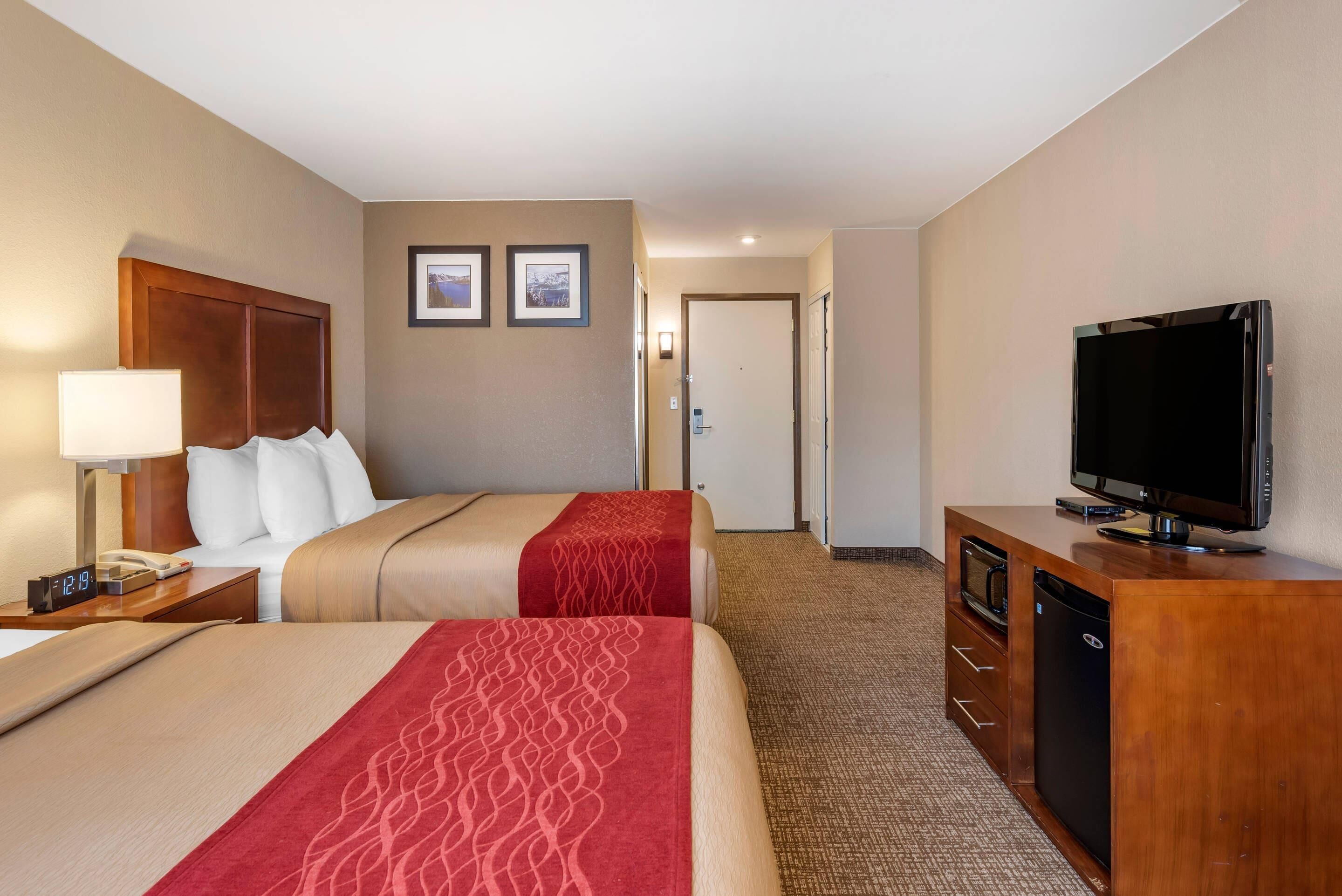 Une chambre d’hôtel avec deux lits, une télévision, un bureau avec une lampe et une porte donnant sur une autre pièce.