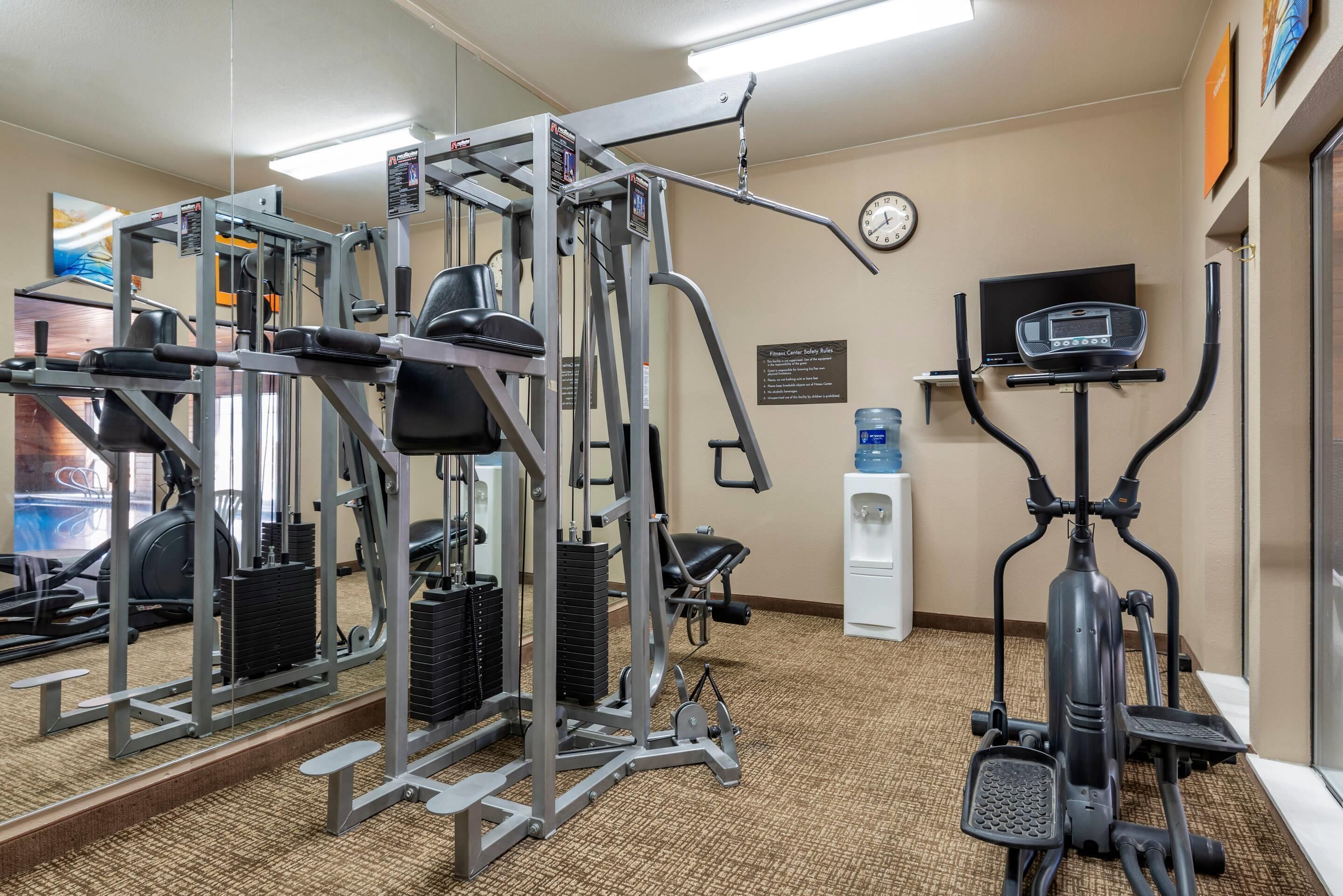 A gym with exercise equipment, a water dispenser, a clock, and a television.