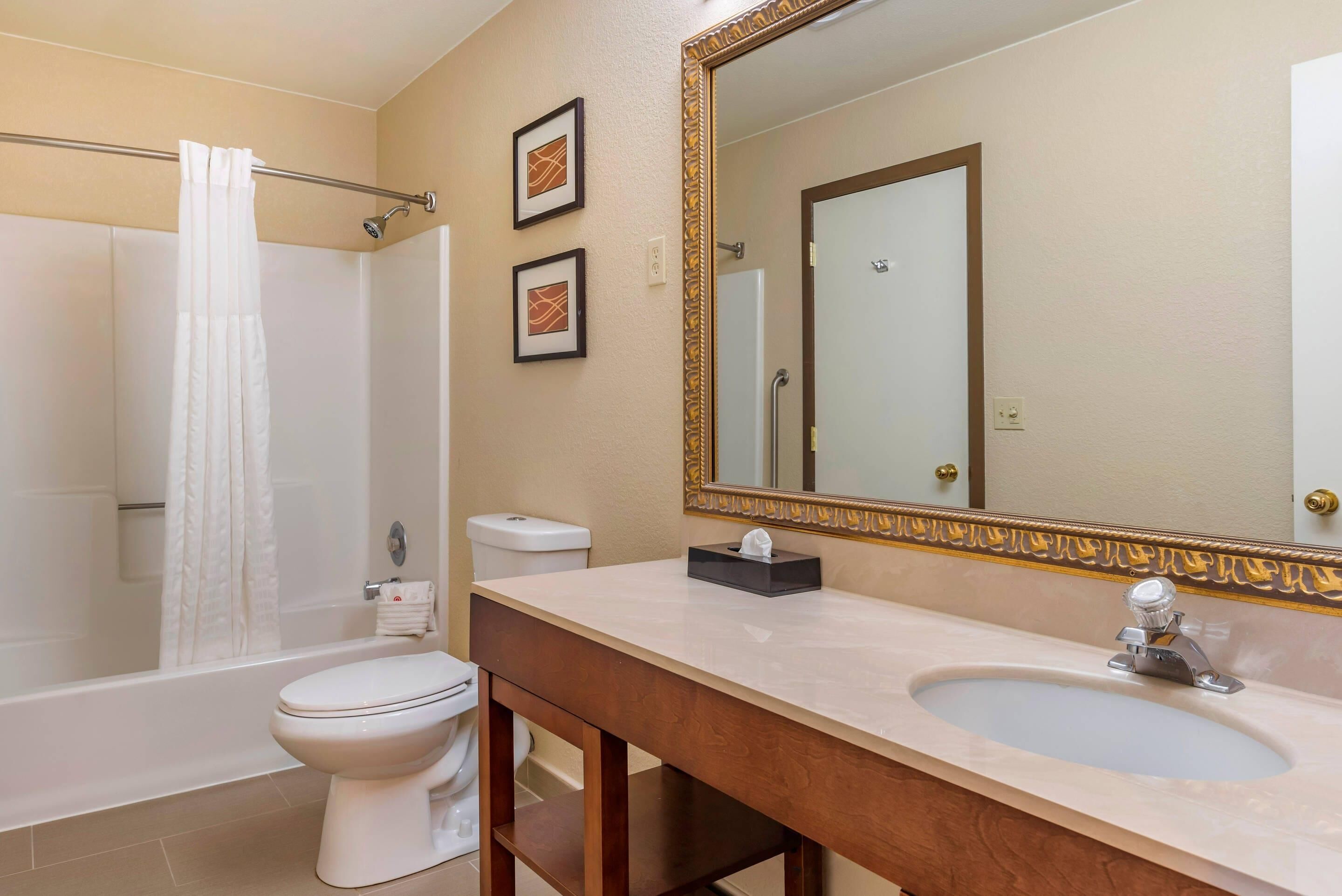 A bathroom with a bathtub, toilet, sink, and a large mirror with a decorative frame.