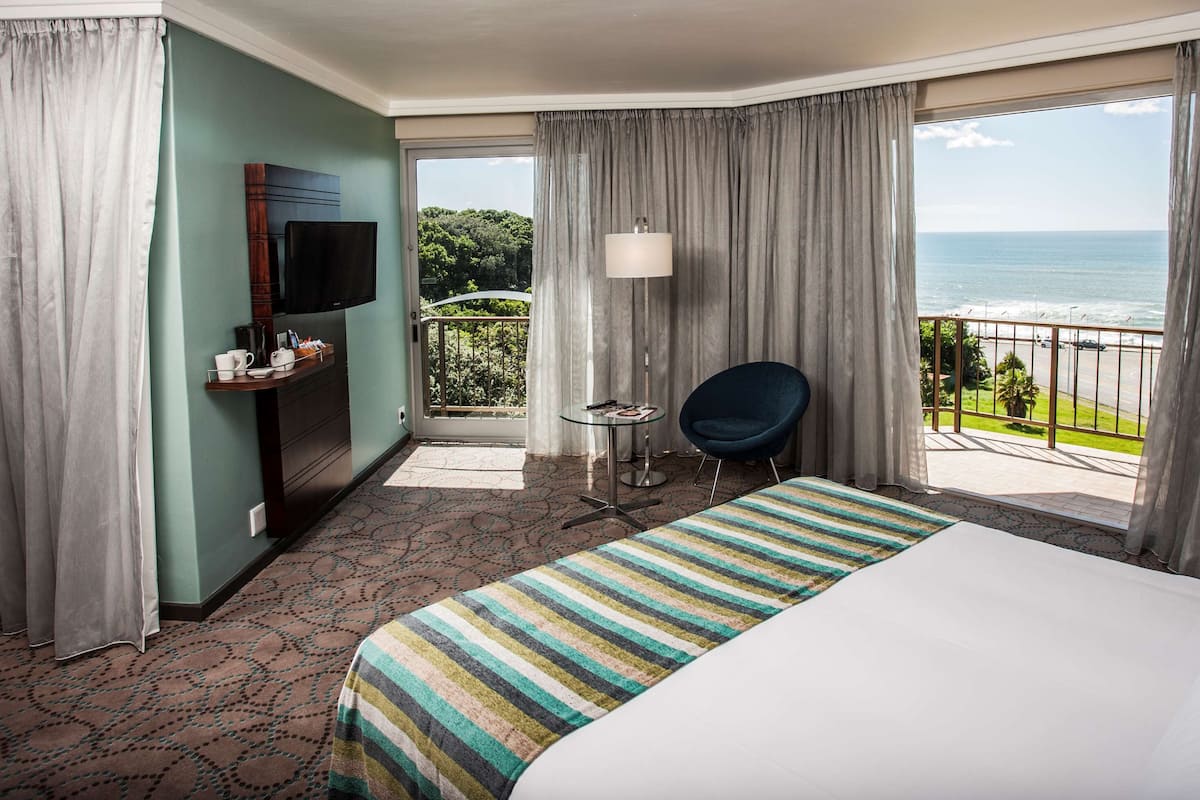 Une chambre d’hôtel comprenant un lit, une télévision, un bureau avec une chaise et un balcon donnant sur l’océan.