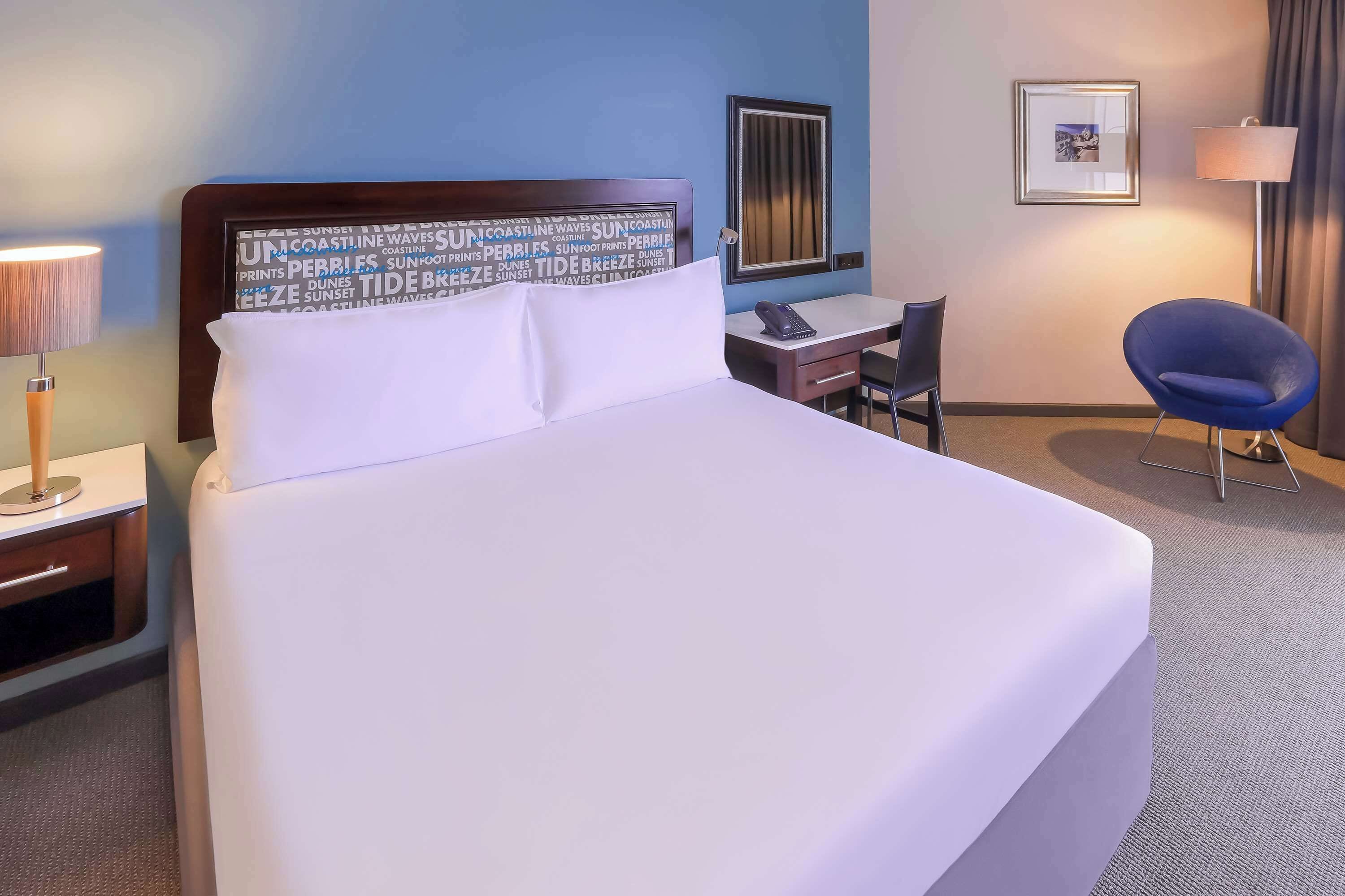 Une chambre d’hôtel avec un grand lit, un bureau, une chaise, une lampe et un tableau encadré au mur.