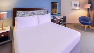 Une chambre d’hôtel avec un grand lit, un bureau, une chaise, une lampe et un tableau encadré au mur.