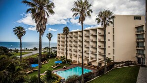 Un hotel con piscina, palmeras y vista al océano.