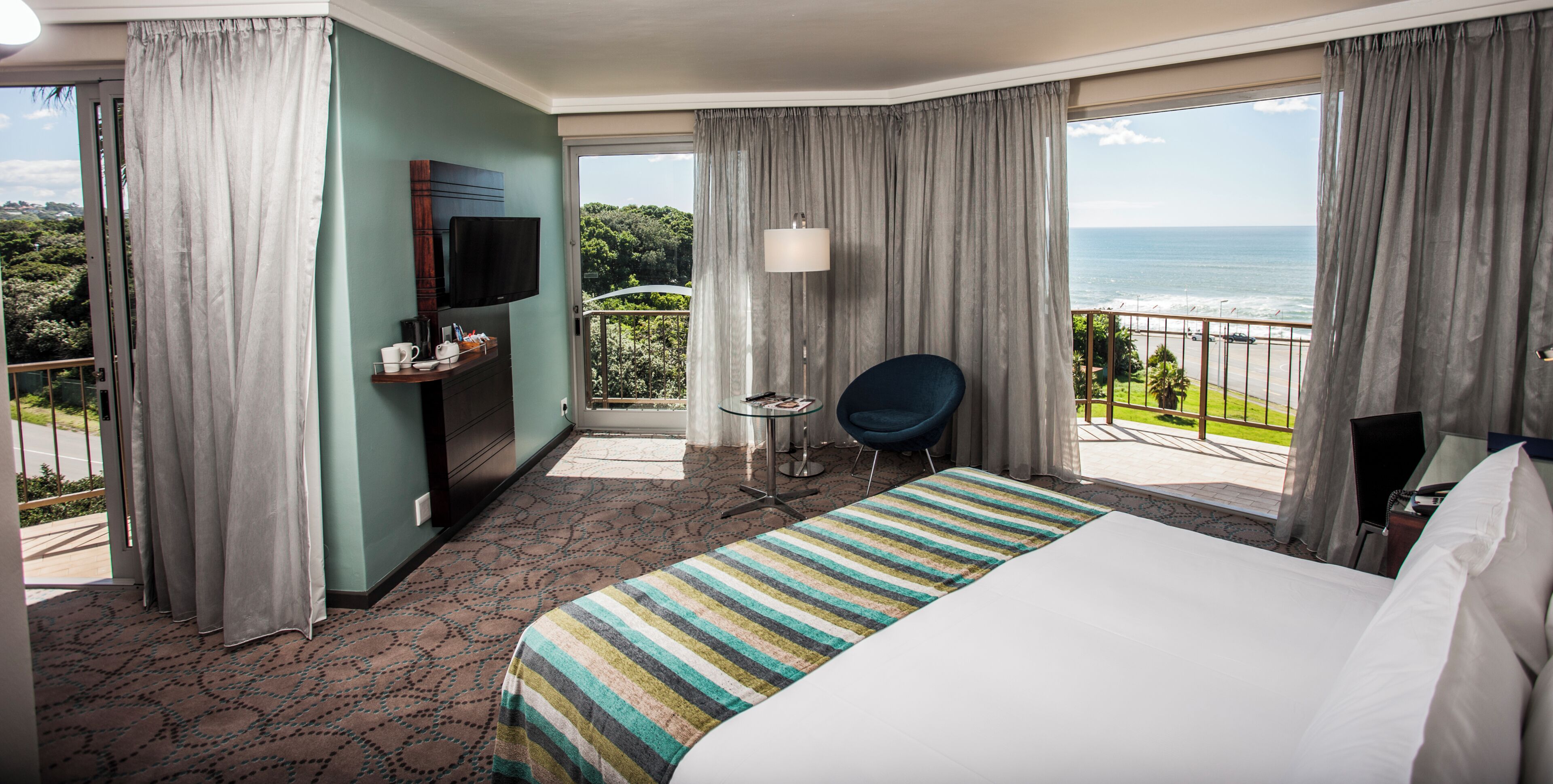 Une chambre d’hôtel avec un lit, une télévision, une chaise, une table et un balcon donnant sur l’océan.