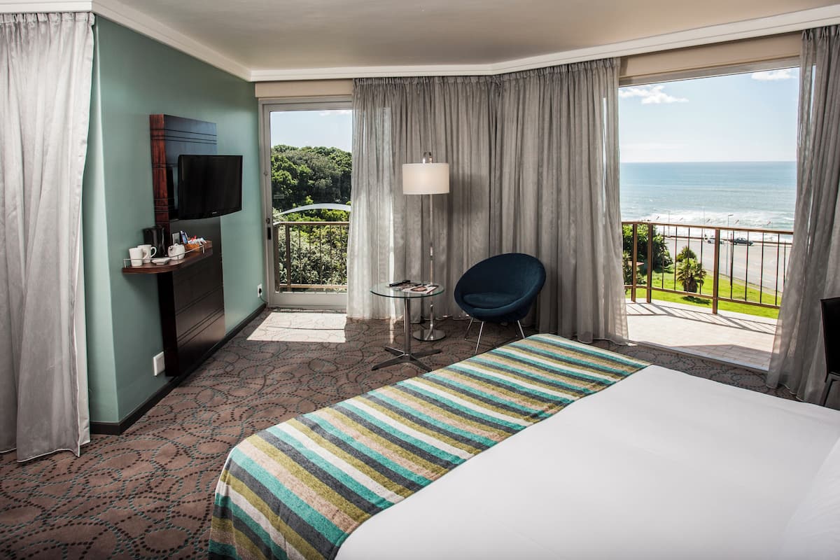 Une chambre d’hôtel avec un lit, une télévision, une chaise, une table et un balcon donnant sur l’océan.