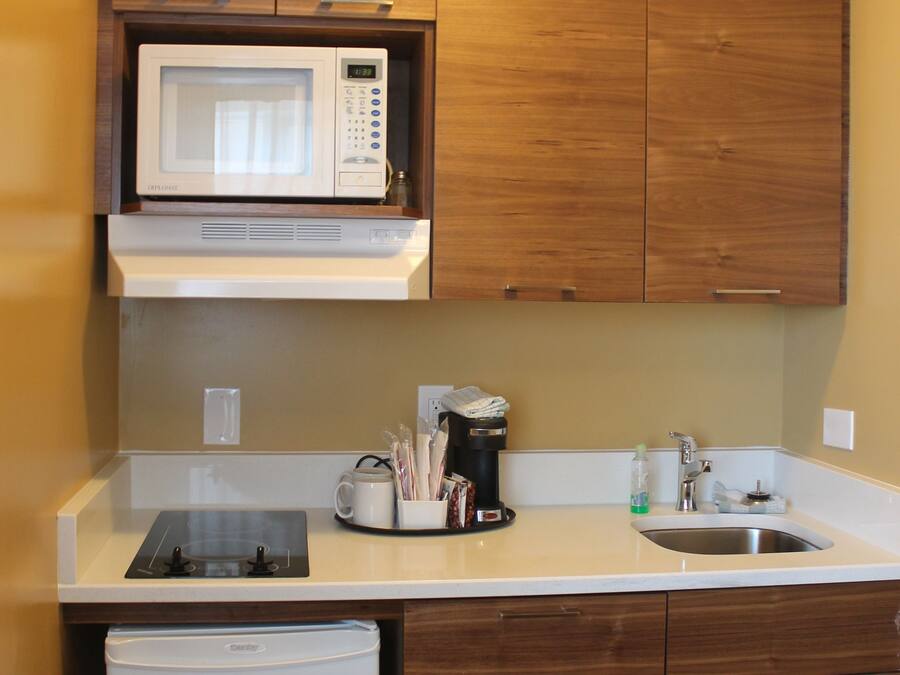 Una cocina compacta con armarios de madera, microondas integrado, cafetera y lavavajillas.