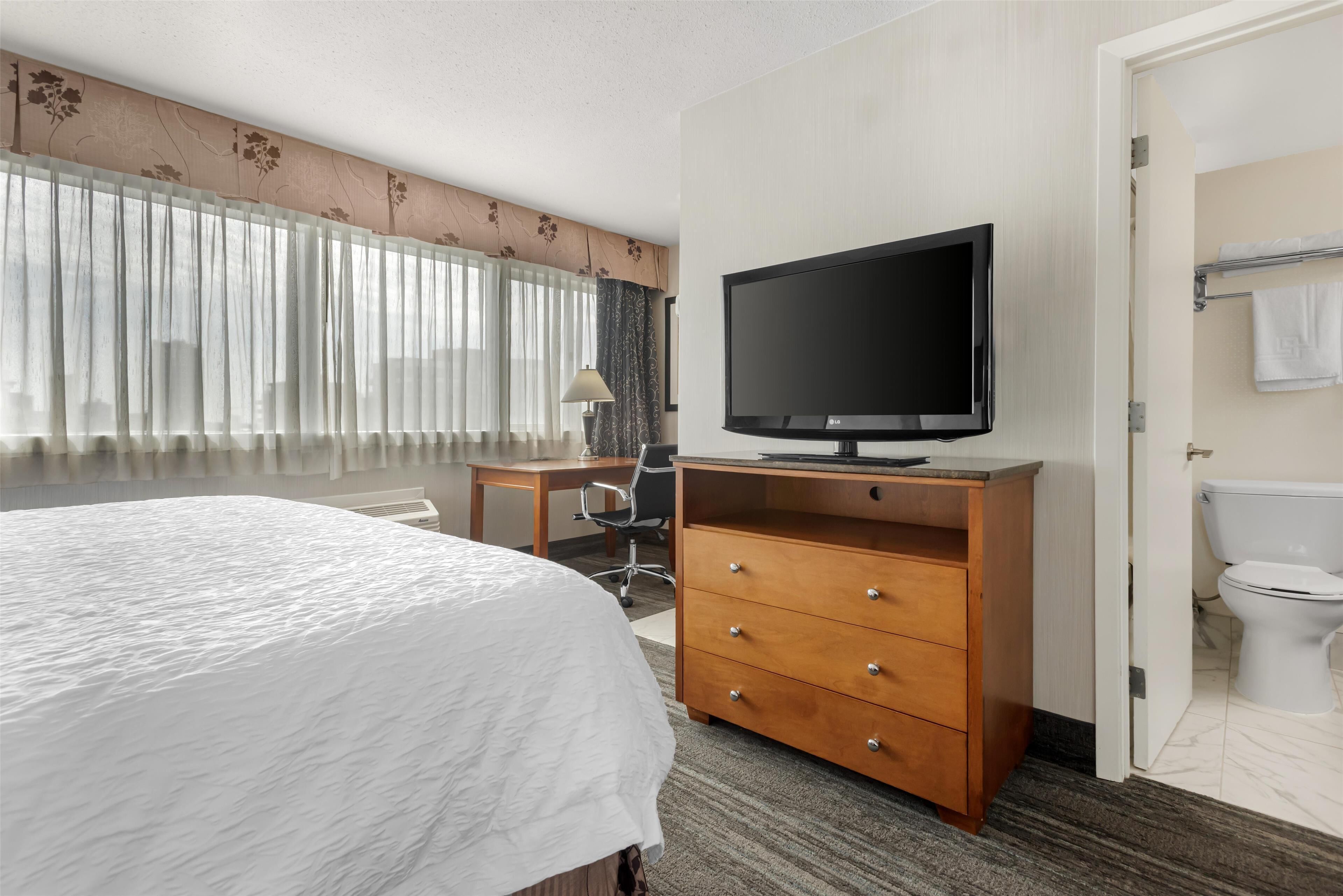 Een hotelkamer met een bed, een bureau met een televisie, een stoel en een badkamer met toilet en handdoekhouder.