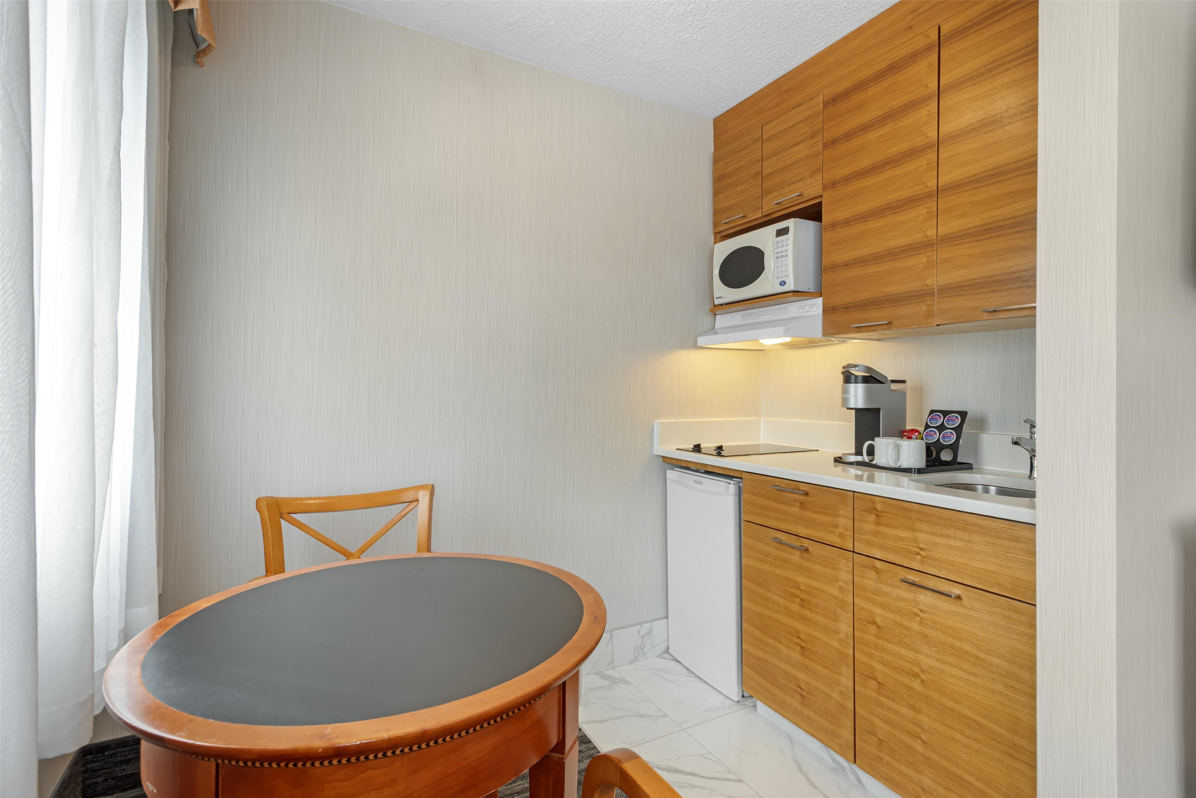 A compact kitchen with wooden cabinets, a microwave, a coffee machine, and a small refrigerator.