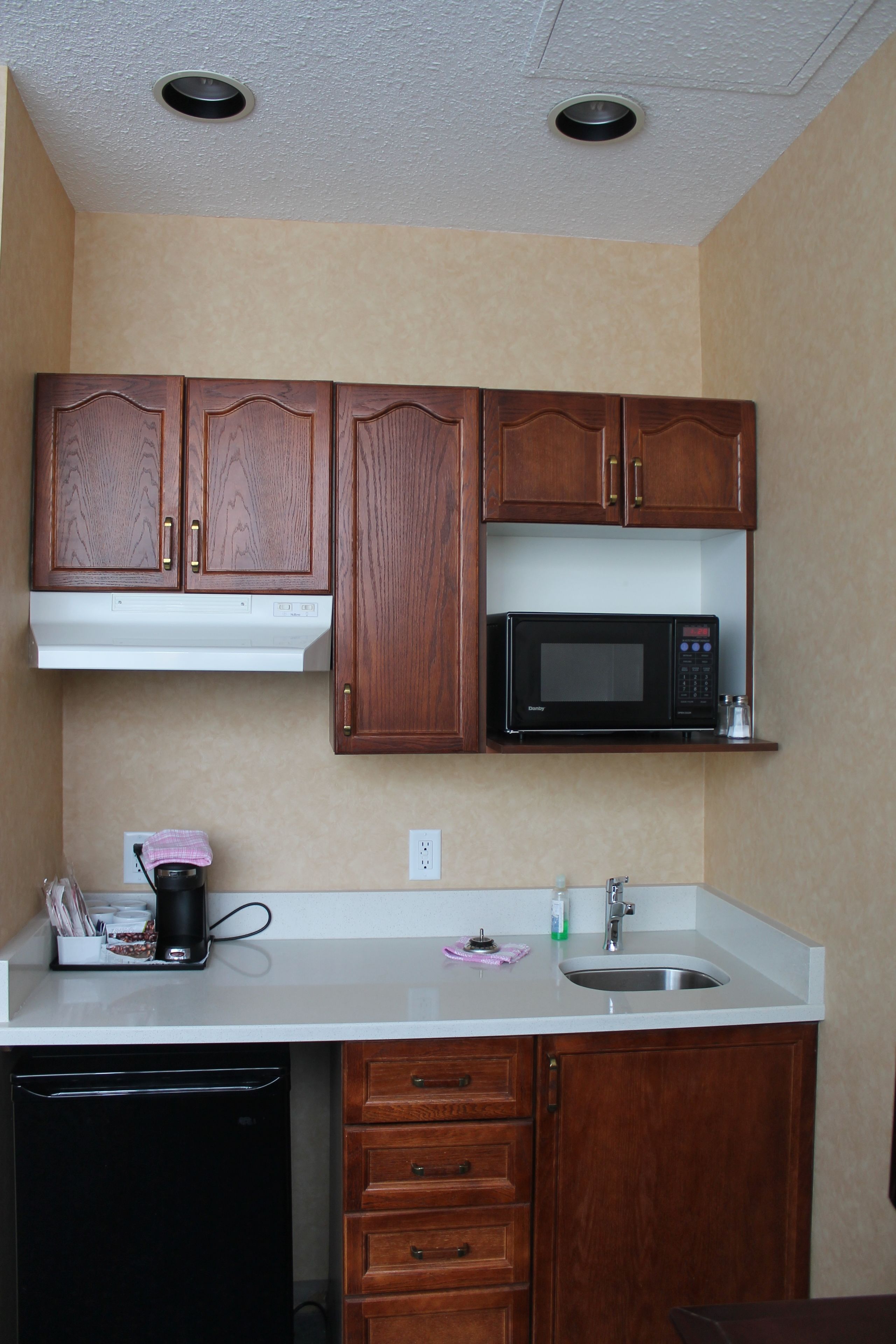 A compact kitchen with wooden cabinets, a microwave, a dishwasher, and a sink.