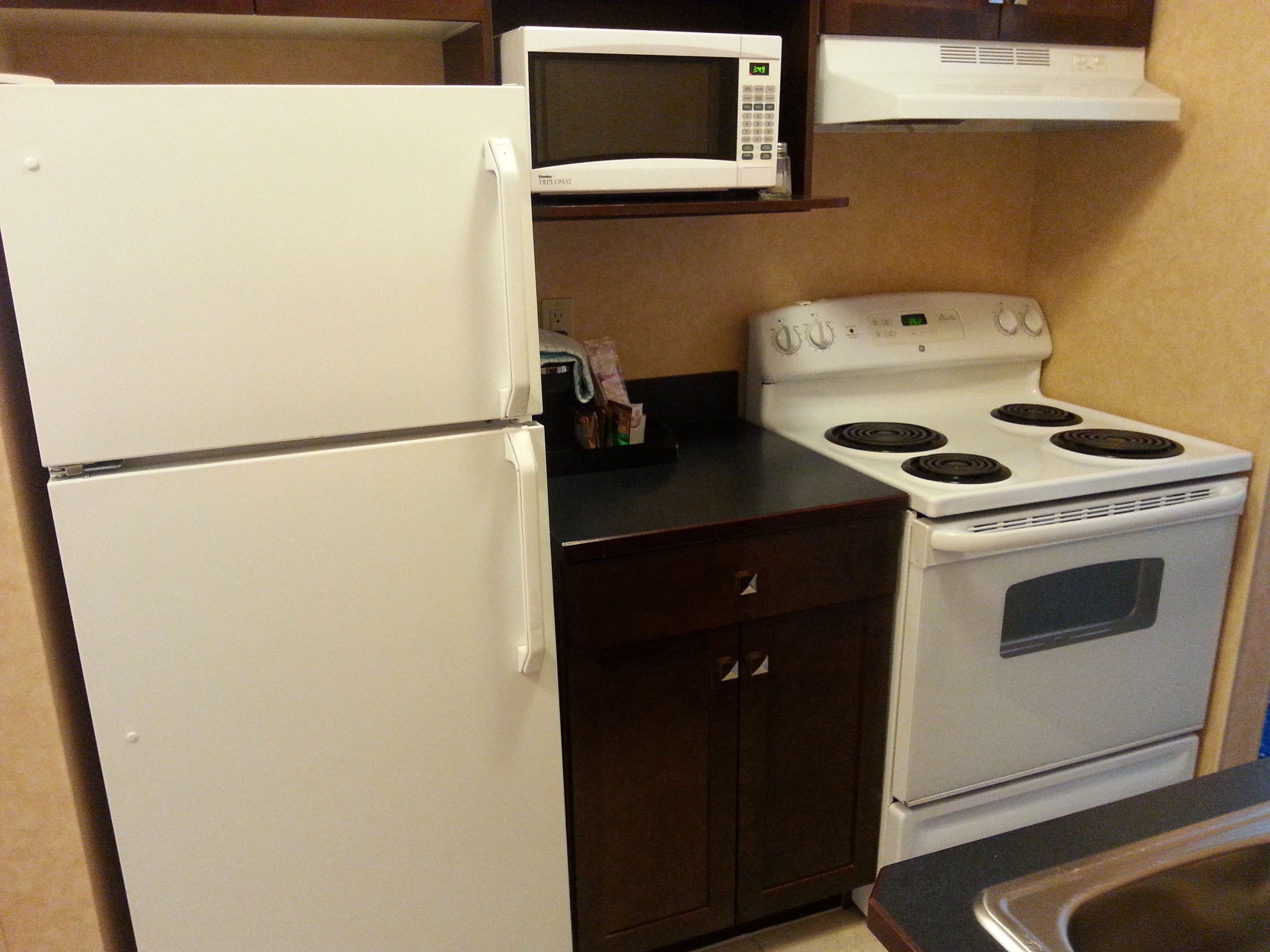 A compact kitchen with a refrigerator, microwave, stove, and dark wooden cabinets.