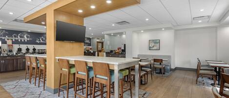 A modern restaurant with a bar area, wooden chairs, and a patterned rug.