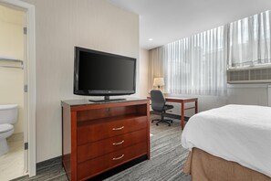 Habitación de hotel con cama, escritorio con computadora, televisor y ventana con cortinas.