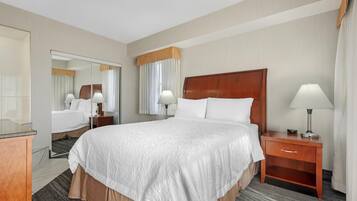 A hotel room with a large bed, a wooden headboard, a nightstand with a lamp, a mirror, and a window with curtains.