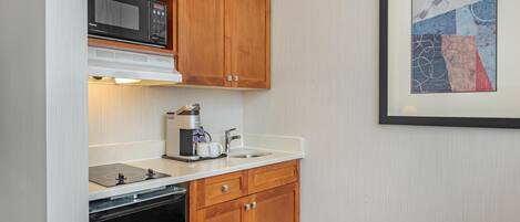 Cocina compacta con armarios de madera, microondas, cafetera y lavabo.