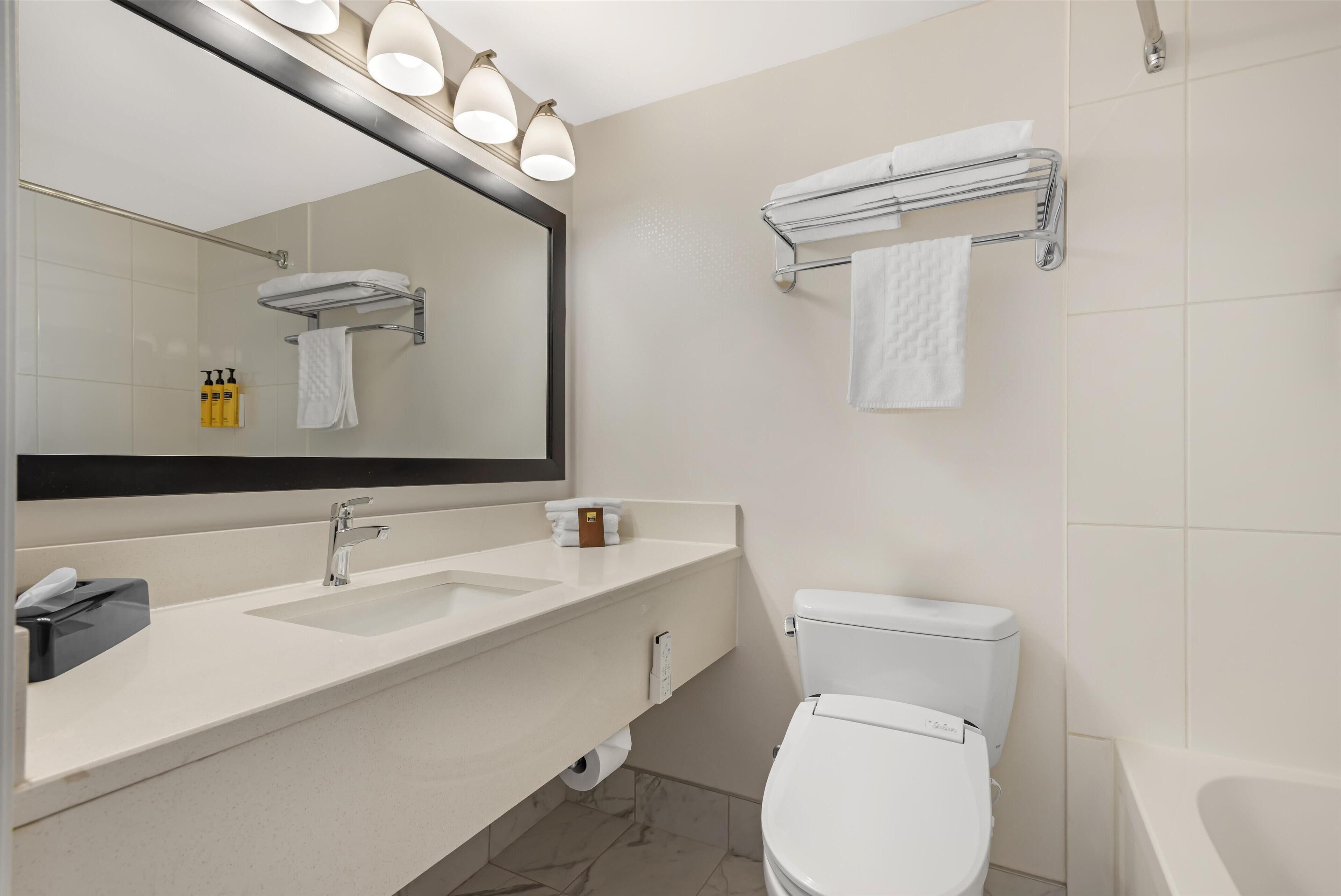 A modern bathroom with a white sink, a mirror, a toilet, and a bathtub.
