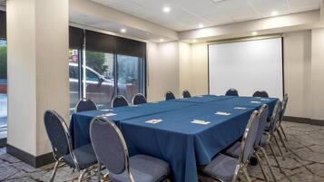 Un salón de conferencias con una larga mesa, sillas y una pantalla para proyector.