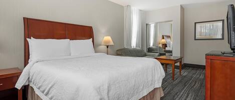 Una habitación de hotel con una cama grande, un escritorio, una silla, un televisor y un espejo.