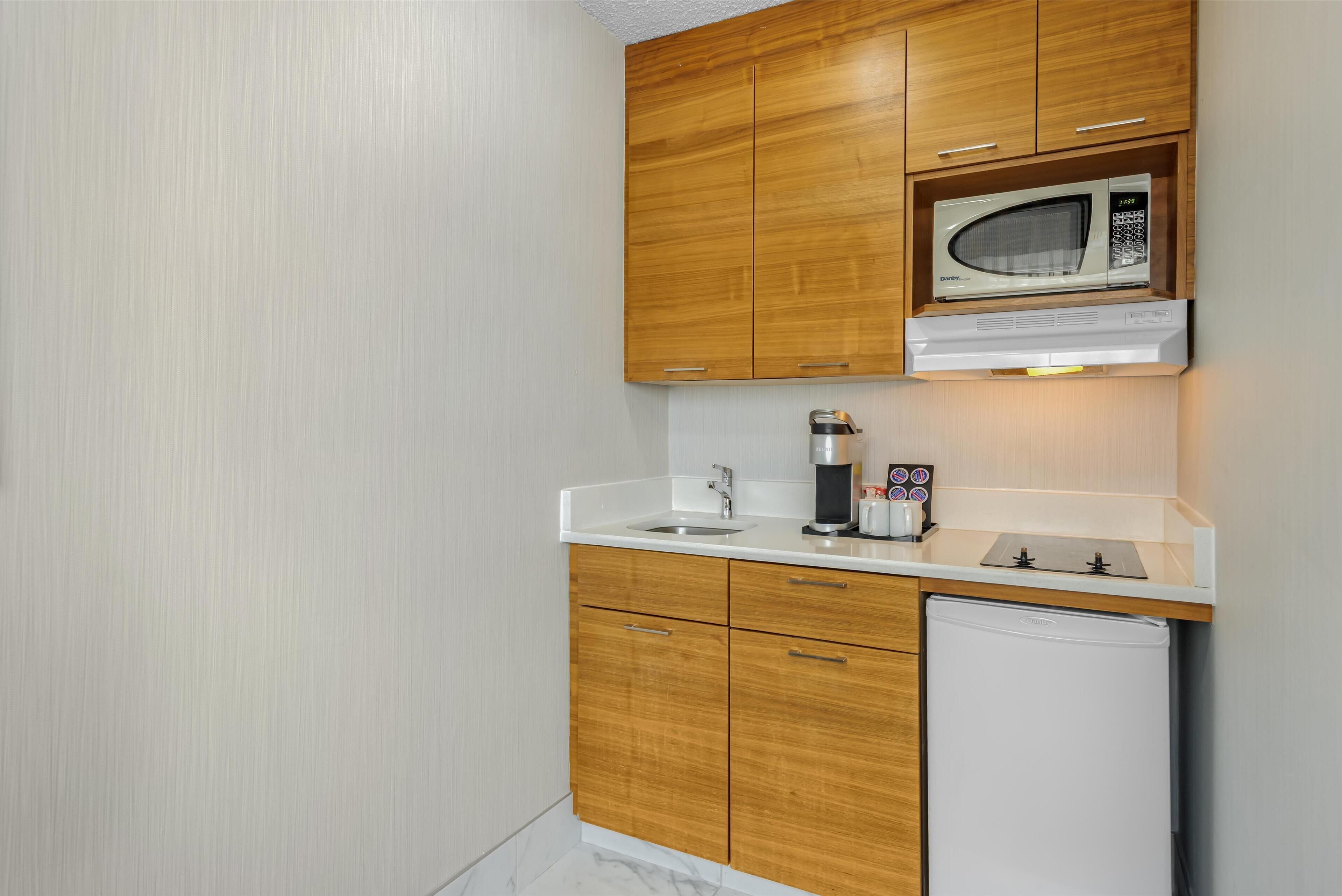 A compact kitchen with wooden cabinets, a built-in microwave, a coffee maker, and a small refrigerator.