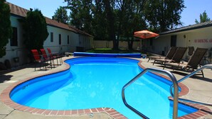 A swimming pool with a brick border, surrounded by lounge chairs and a covered umbrella. - Sunrise Motor Inn (Cody)