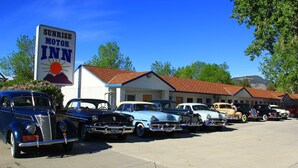 A motel with a large sign, vintage cars parked in front, and a building with a red roof. - Sunrise Motor Inn (Cody)