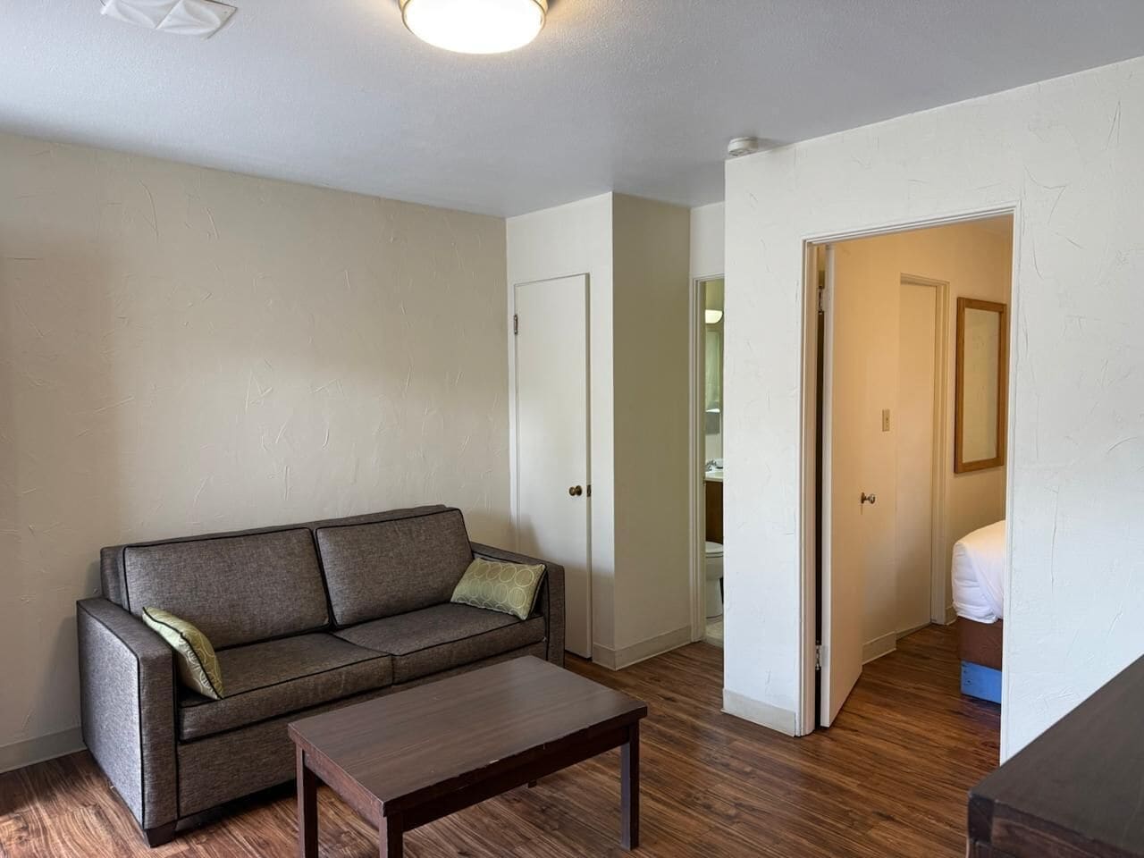 Una sala de estar con sofá, una mesa de centro y una puerta que da a un dormitorio.