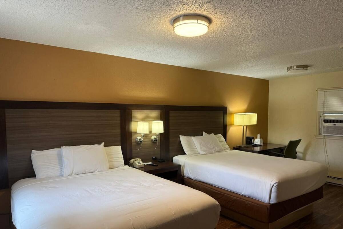 Habitación de hotel con dos camas, una mesita de noche, una lámpara y una luz en el techo.