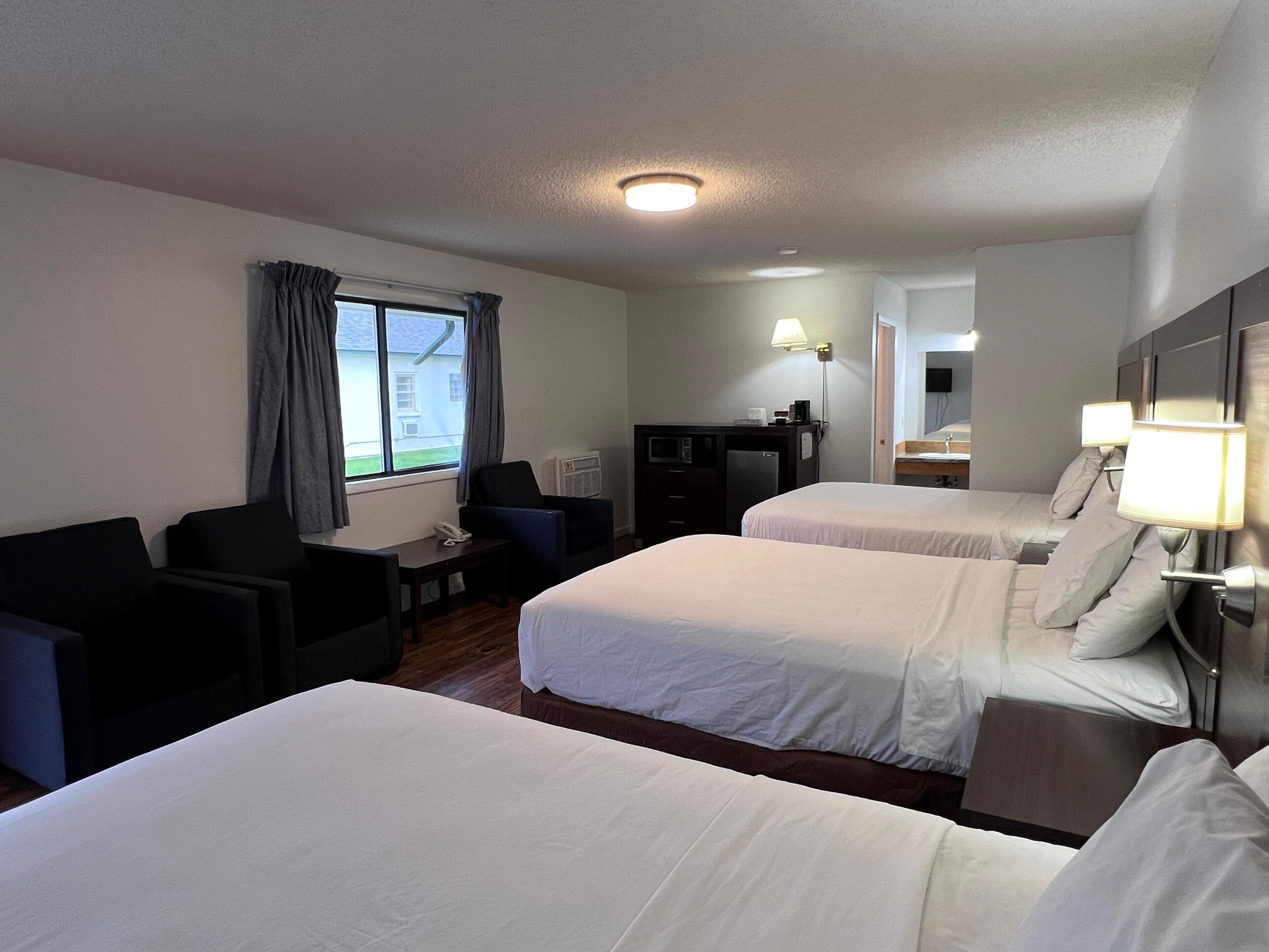 A hotel room with two beds, a desk, a chair, a desk lamp, and a window with curtains.