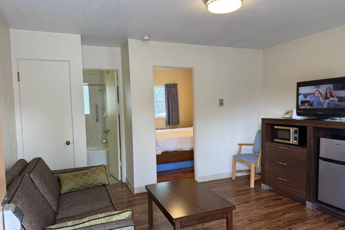 Habitación de hotel compacta con sofá, una mesita, microondas, refrigerador y televisor.