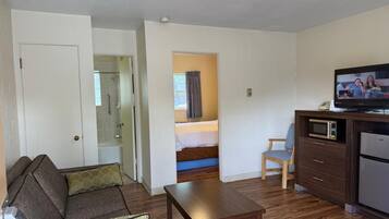 Habitación de hotel compacta con sofá, una mesita, microondas, refrigerador y televisor.