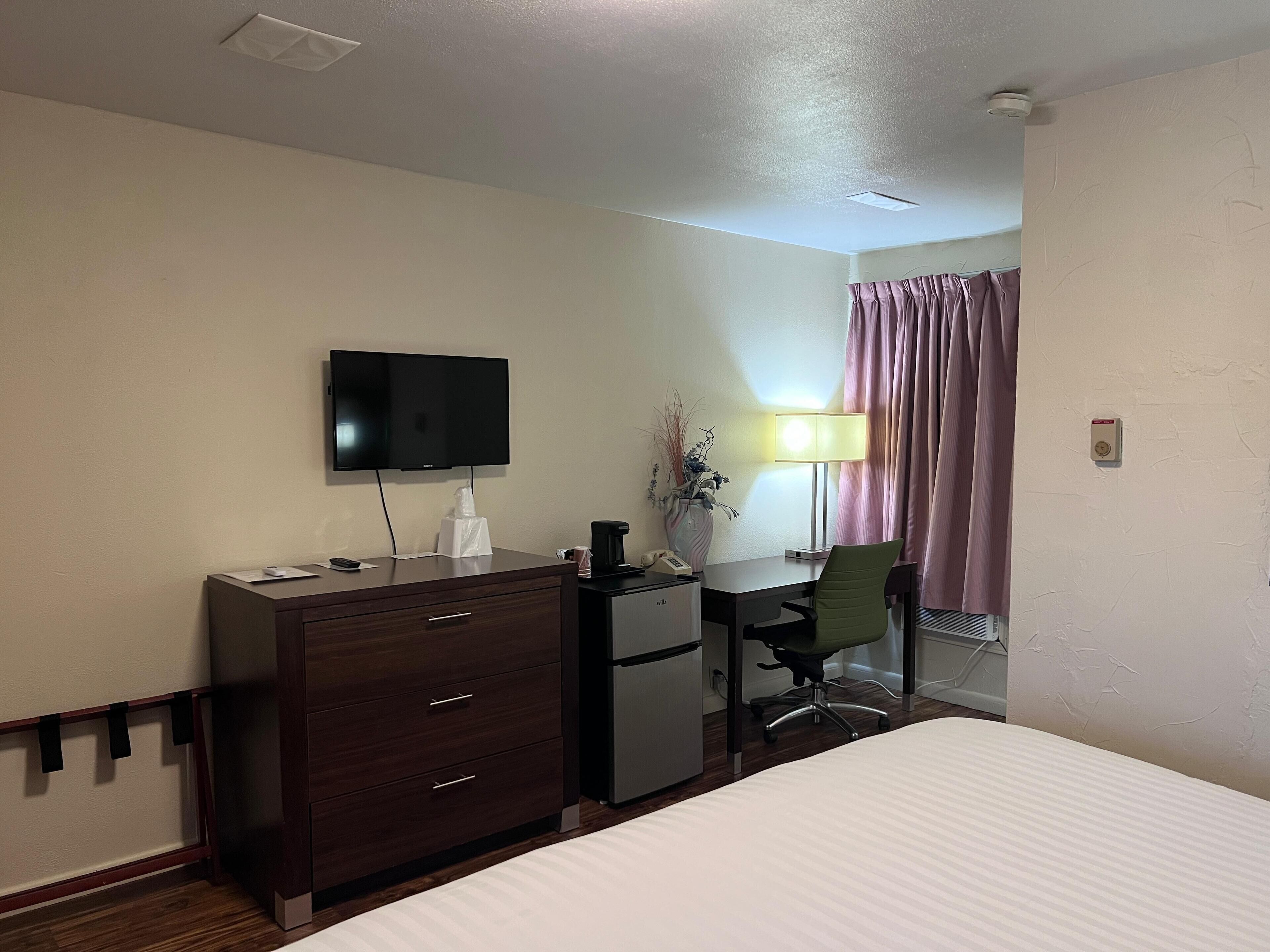 A hotel room with a bed, a desk with a computer, a television, a lamp, and a chair.