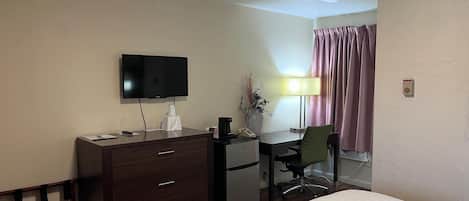 A hotel room with a bed, a desk with a computer, a television, a lamp, and a chair.