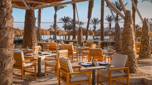 An outdoor dining area with wooden tables and chairs, stone pillars, and palm trees. - JAZ Fayrouz (Sharm El Sheikh)