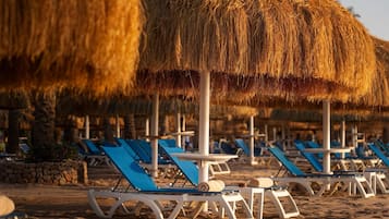 A beach with rows of sun loungers and thatched umbrellas.