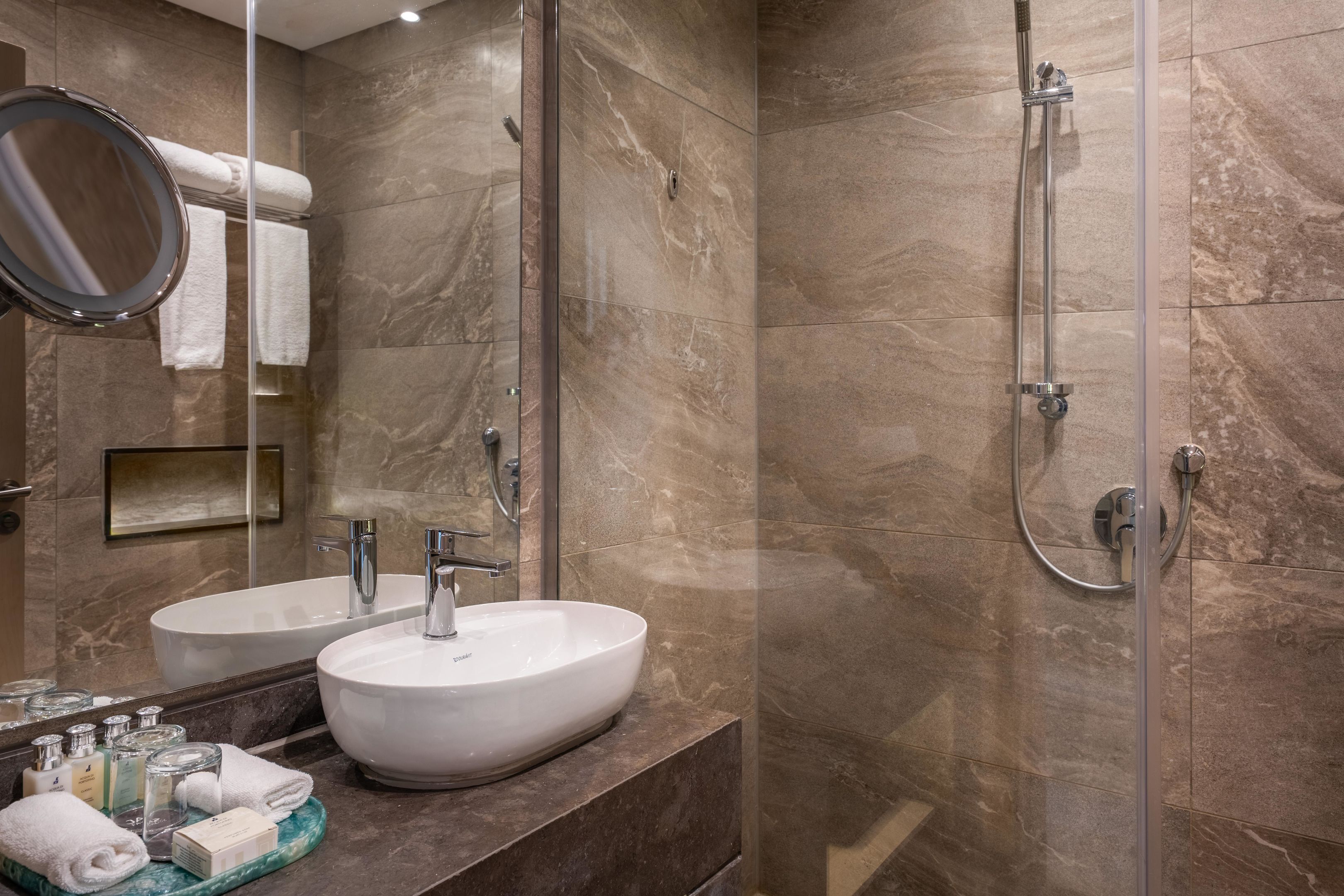 Un baño moderno con dos lavamanos, ducha y cabina de ducha con paredes de vidrio.