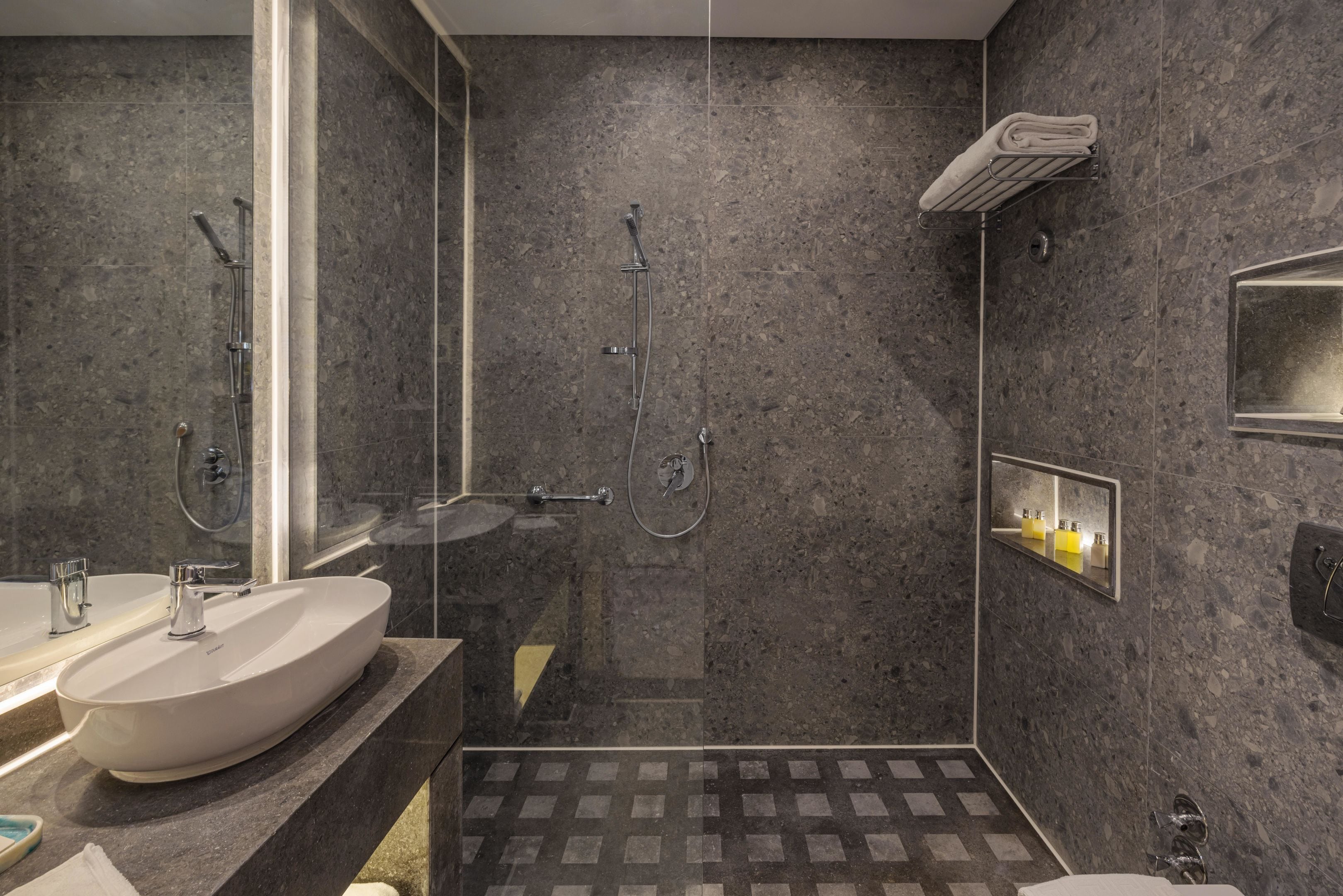 Un baño moderno con un lavamanos ovalado grande, una ducha con cerramiento de vidrio y un espejo pequeño con luz.