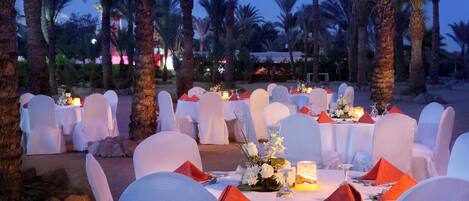 An outdoor dining area with round tables, white chairs, and orange napkins.