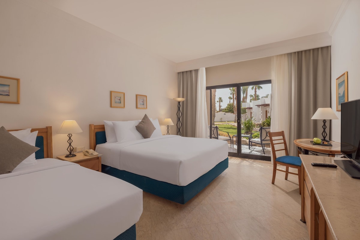 Une chambre d’hôtel avec deux lits, un bureau avec une chaise, une télévision et une vue sur l’extérieur.