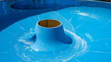 A large, blue swimming pool with a central water slide.