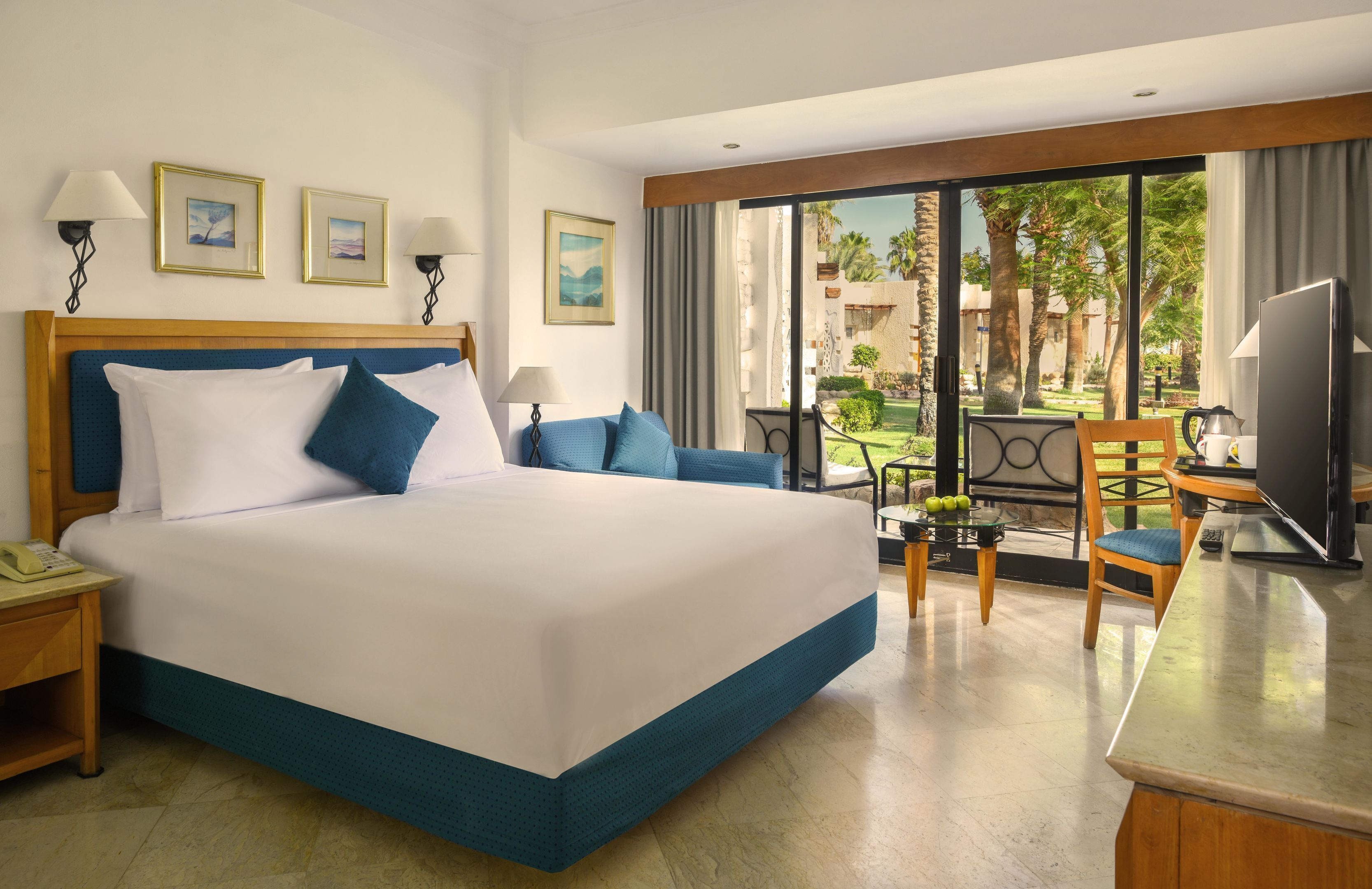 A hotel room with a large bed, a desk with a television, and a view of the outdoors.