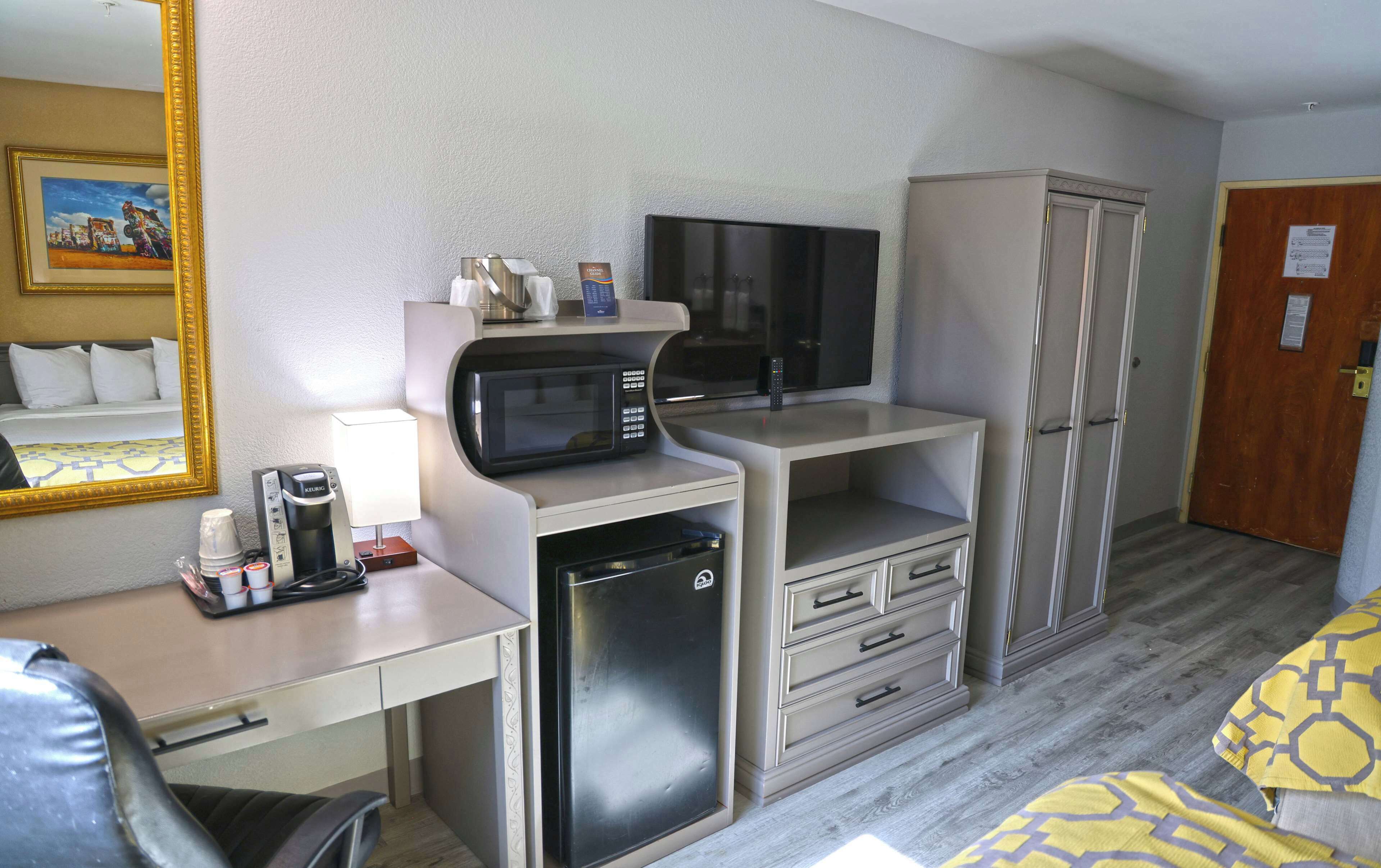 Habitación de hotel con cama, escritorio con microondas, refrigerador, armario y espejo.