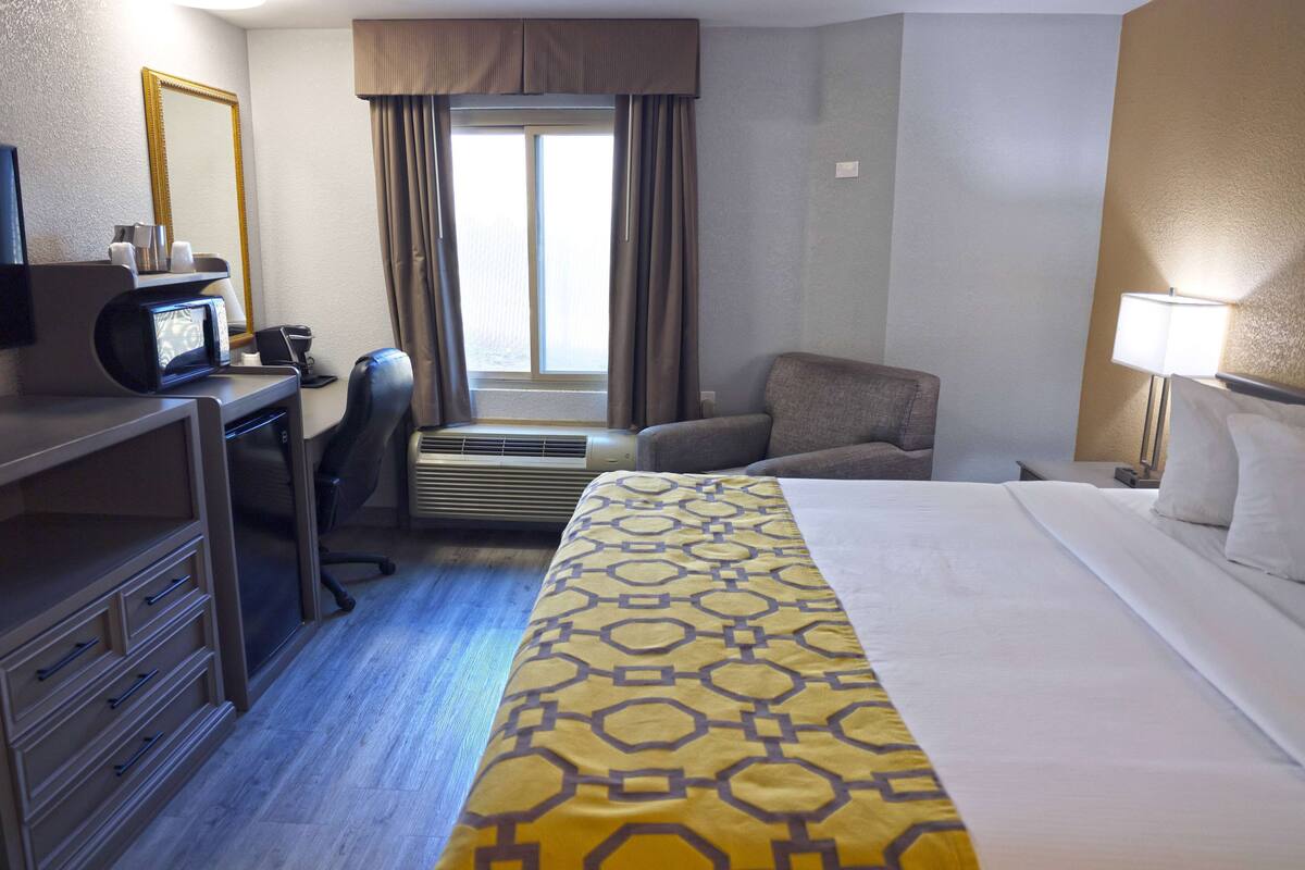 A hotel room with a bed, desk, chair, and a window with curtains.