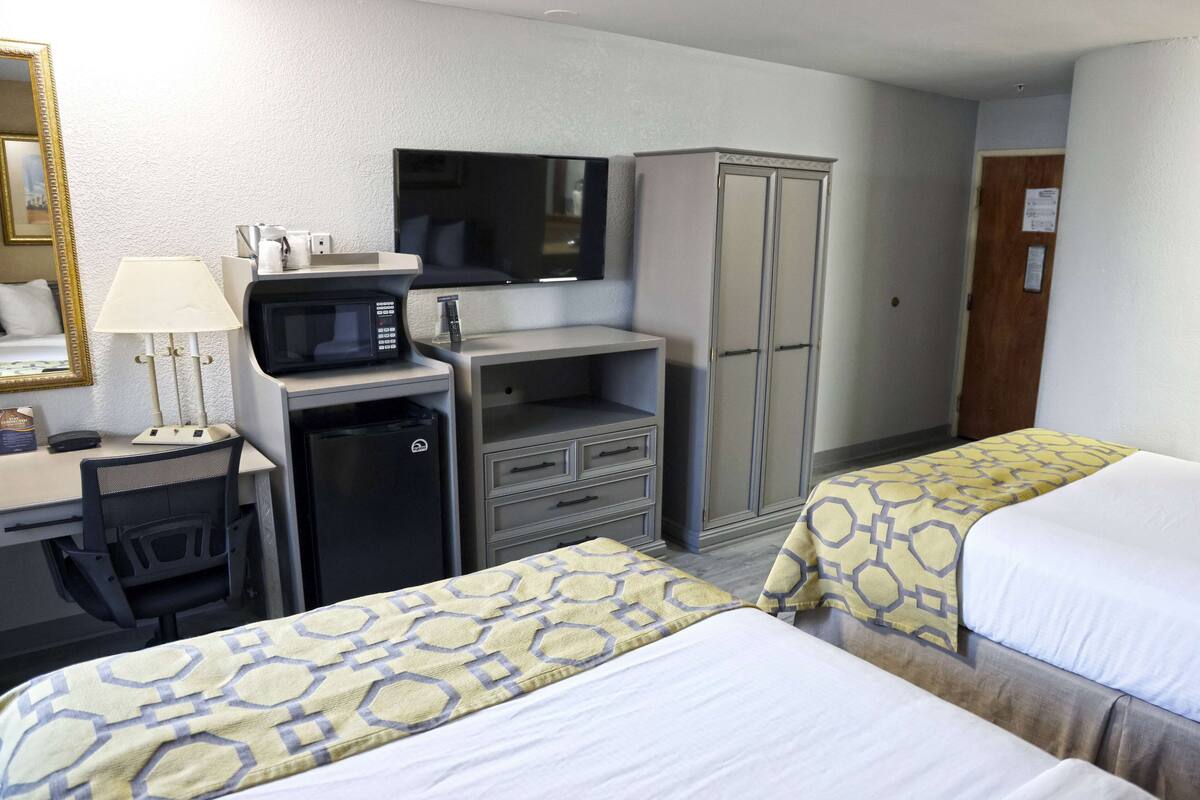 A hotel room with two beds, a desk with a computer, a microwave, a television, and a wardrobe.