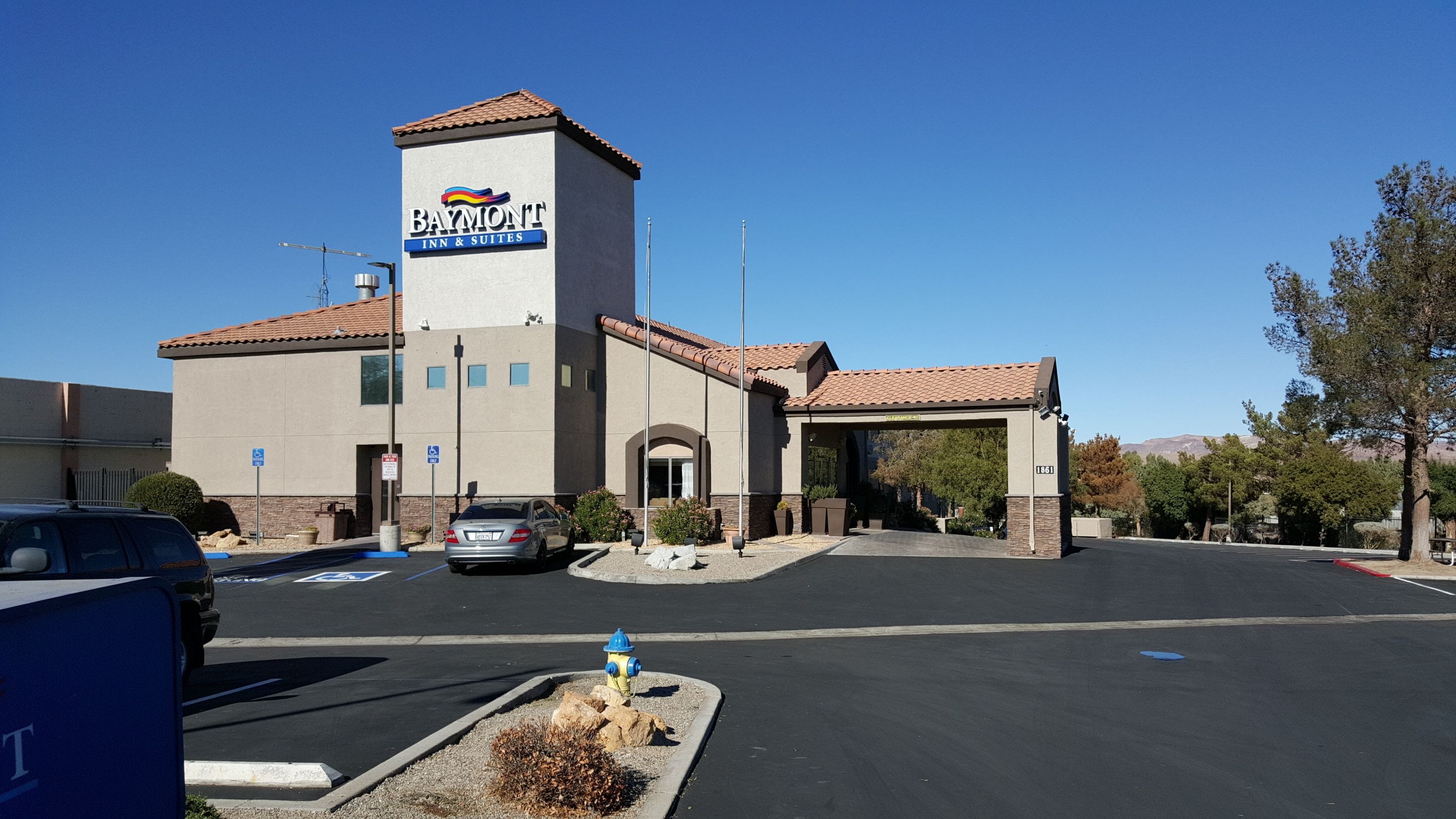 A Baymont Inn & Suites with a parking lot, a fire hydrant, and a clear blue sky.
