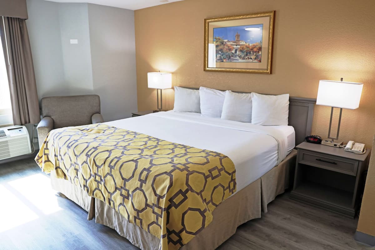 A hotel room with a large bed, two bedside lamps, a nightstand with a phone, a chair, and a painting on the wall.