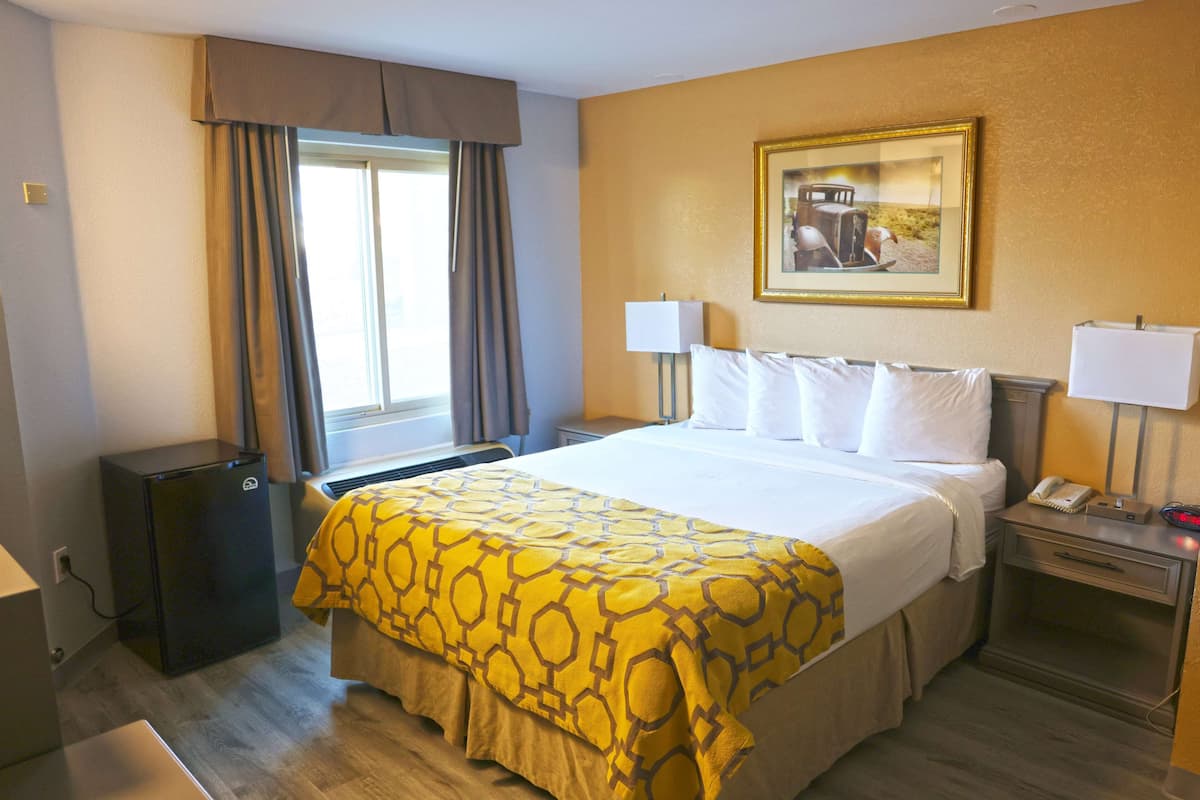 A hotel room with a bed, bedside lamps, a desk, a small table, a window with curtains, and a wall-mounted picture.