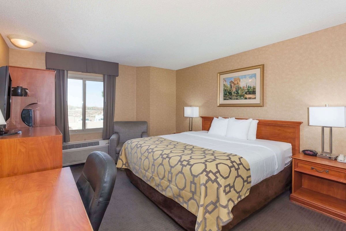 A hotel room with a bed, desk, chair, and a painting on the wall.